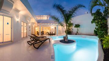 Un área de piscina con sillones de descanso, una piscina pequeña y una zona de estar techada.