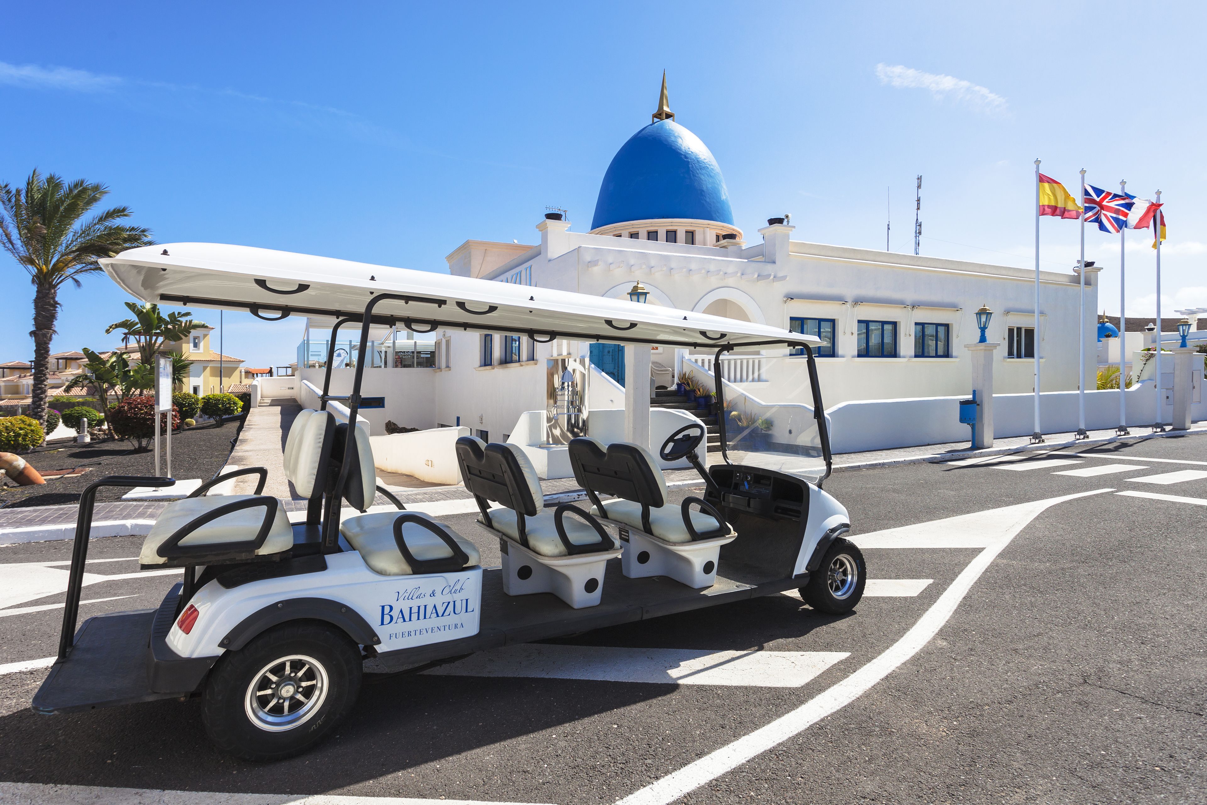 A golf cart with a sign reading "Bahiazul" parked in front of a building with a blue dome and flags.