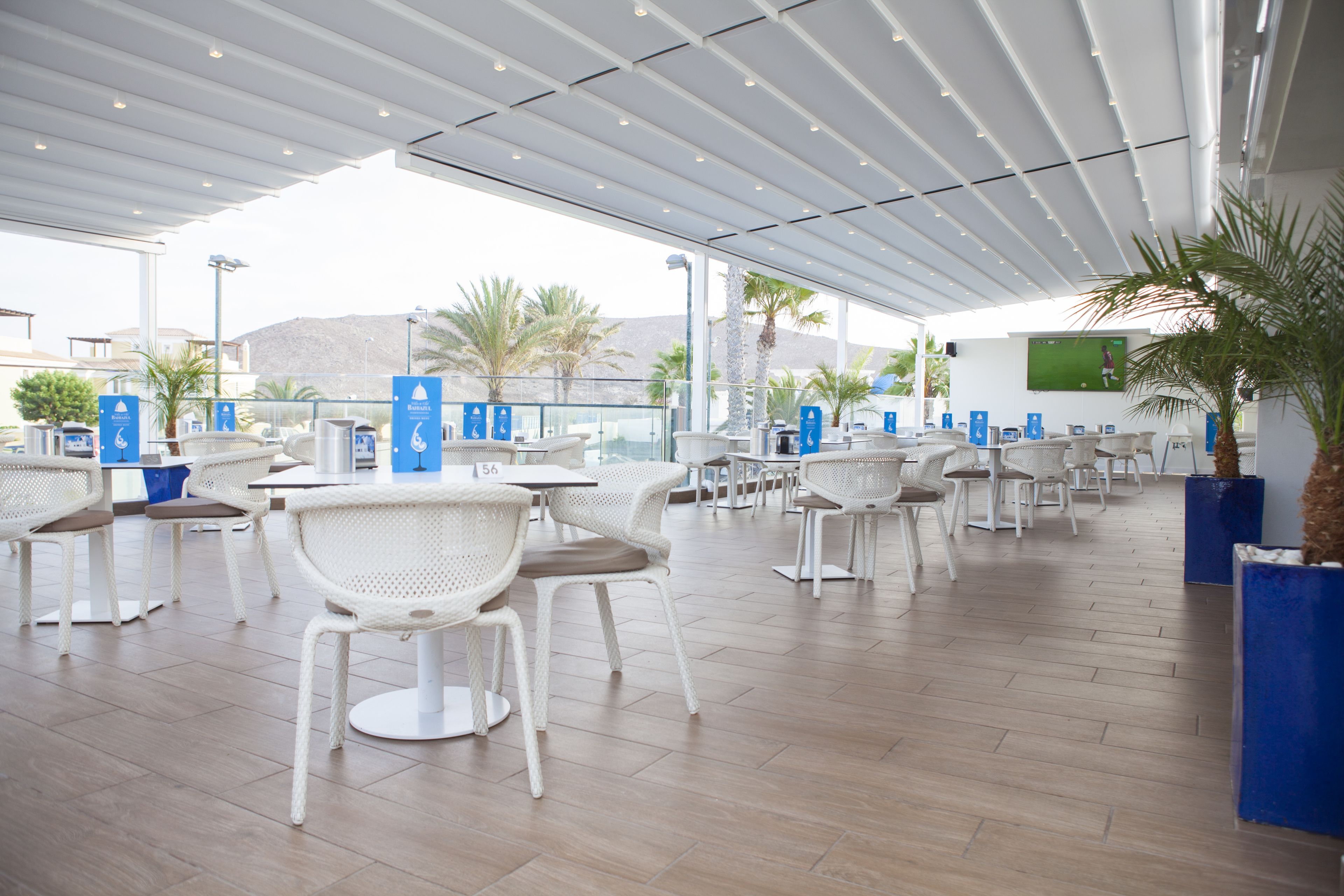 A spacious outdoor seating area with white wicker chairs and tables, a covered roof, and a view of the surrounding landscape.