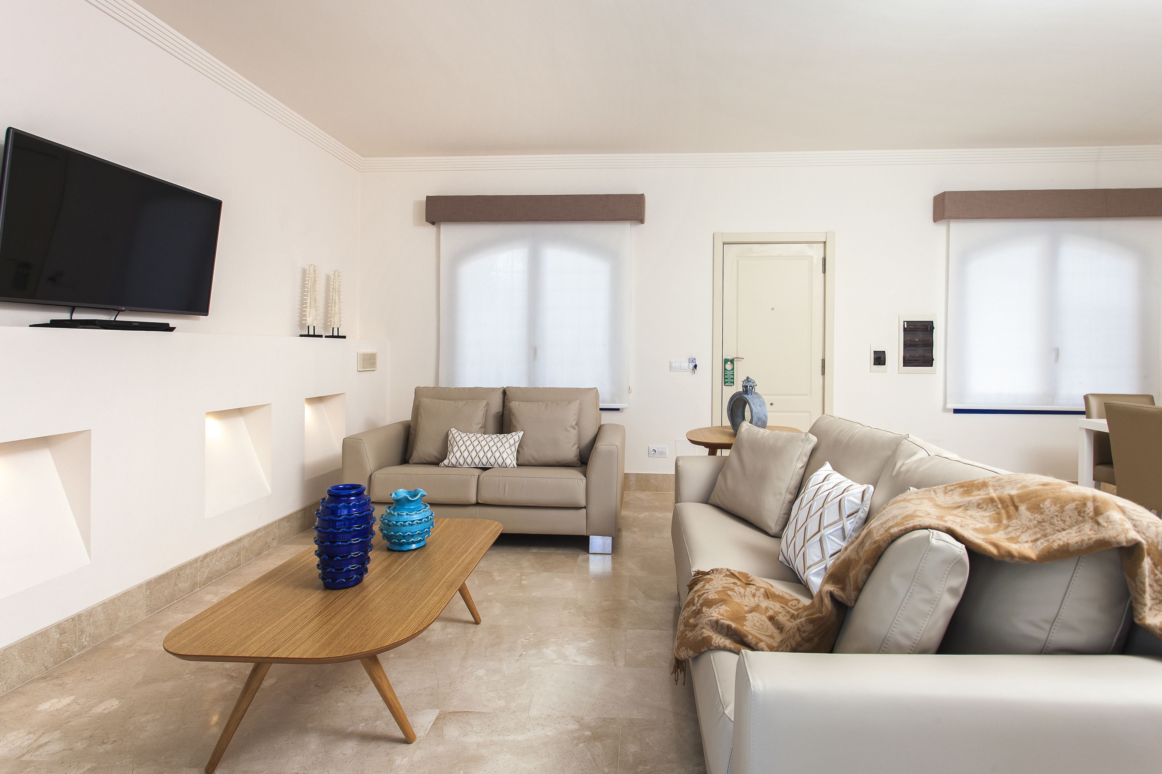 Un salon moderne avec un téléviseur à écran plat, deux canapés, une table basse et une porte visible au fond.