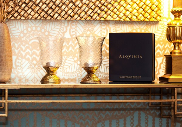 A set of two crystal goblets on a gold tray, a black box with gold lettering, and a golden trophy on a table with patterned wallpaper.