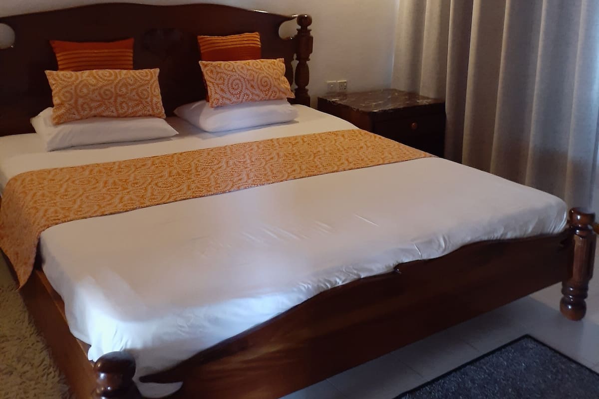 A neatly made bed with a wooden headboard, a nightstand with a lamp, and a painting of an underwater scene on the wall.