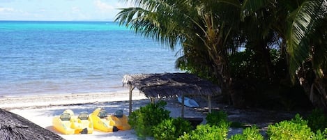 A beach with a thatched-roof structure, yellow inflatable boats, and palm trees.