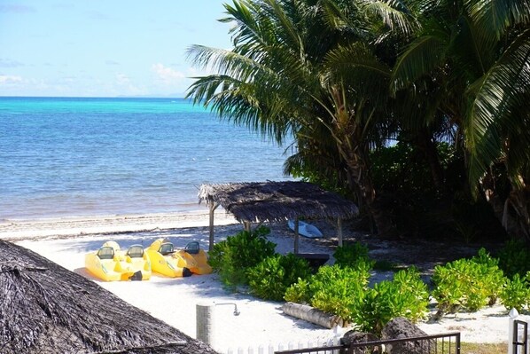 Una playa con una estructura de techo de paja, botes inflables amarillos y palmeras.