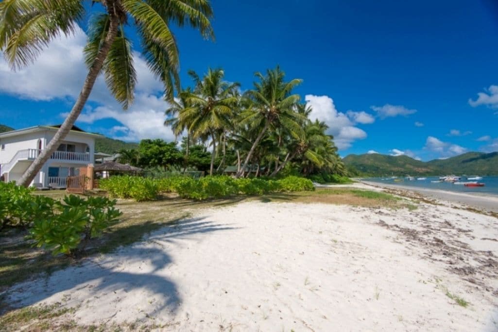 A beachfront property with a white house, palm trees, and a sandy beach.