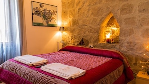 Un dormitorio con pared de piedra, una cama con colcha roja y marrón, y un cuadro de flores en la pared.