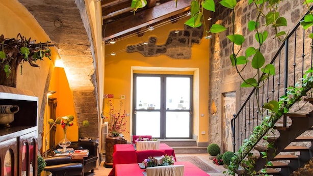 Un interior con pared de piedra, una escalera y mesas con manteles rojos.