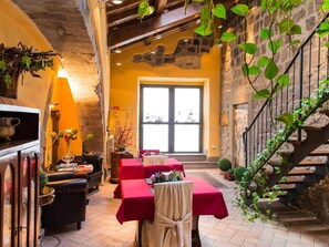An interior with a stone wall, a staircase, and tables with red tablecloths. - Medieval House (Viterbo)