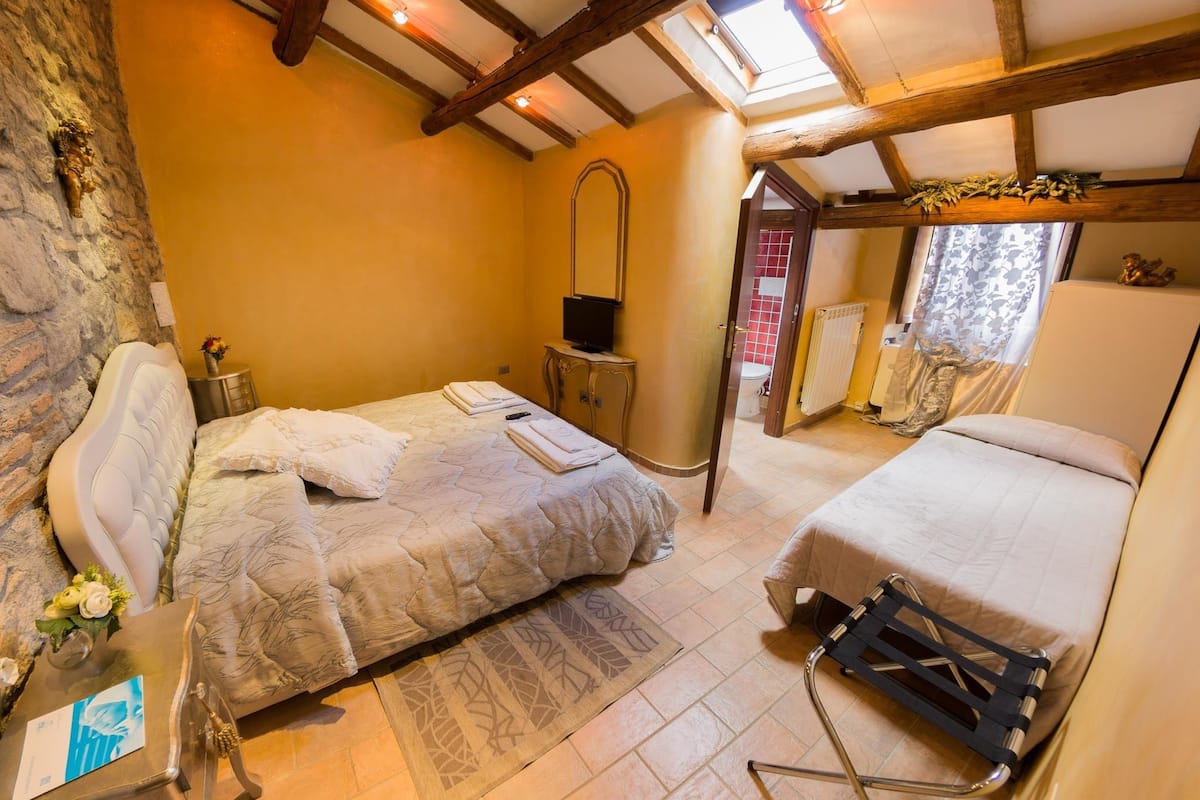 A bedroom with two beds, a stone wall, a wooden ceiling, and a skylight.