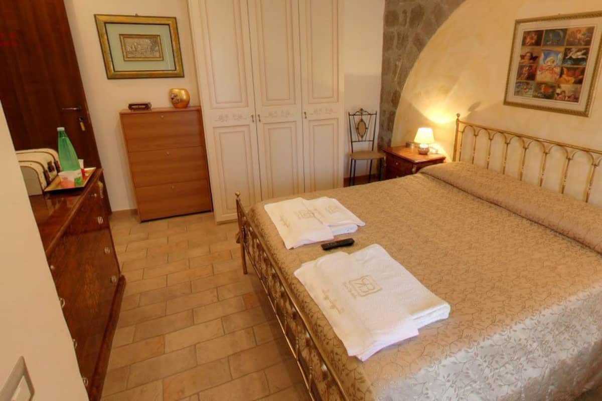 A bedroom with a bed, a dresser, a chair, and a nightstand with a lamp.