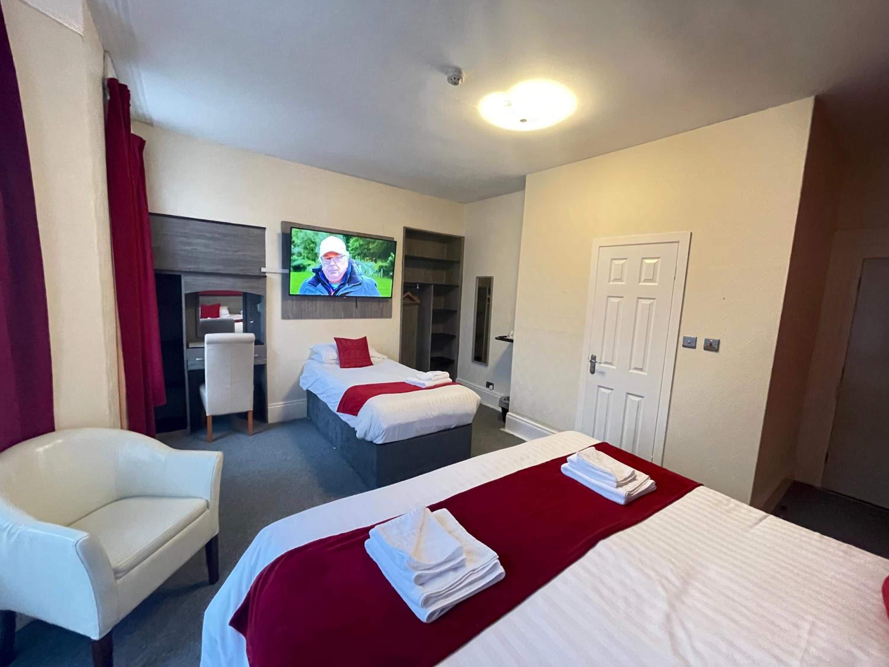 Een hotelkamer met twee bedden, een bureau, een stoel en een televisie aan de muur.