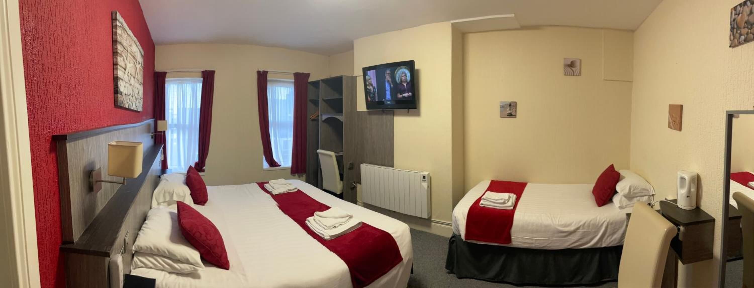 Een hotelkamer met twee bedden, een televisie, een bureau en een raam met gordijnen.