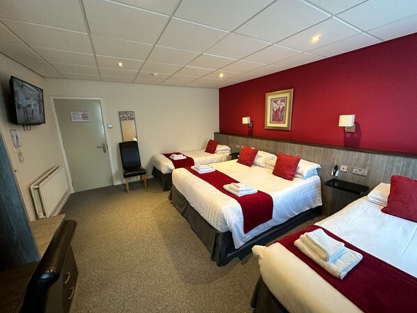 A hotel room with two beds, a desk, a chair, a television, and a red accent wall.