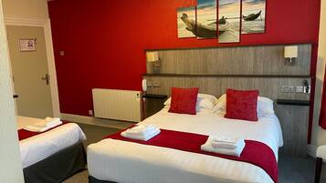 Habitació d'hotel amb una paret vermella, un llit amb roba de llit blanca i nínxols vermells, una taula de nit amb una làmpada, i un quadre d'una embarcació a la paret.