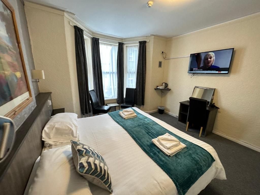 Une chambre d’hôtel avec un lit, un bureau, une chaise, une télévision et une fenêtre avec des rideaux.
