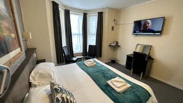 A hotel room with a bed, a desk, a chair, a television, and a window with curtains.