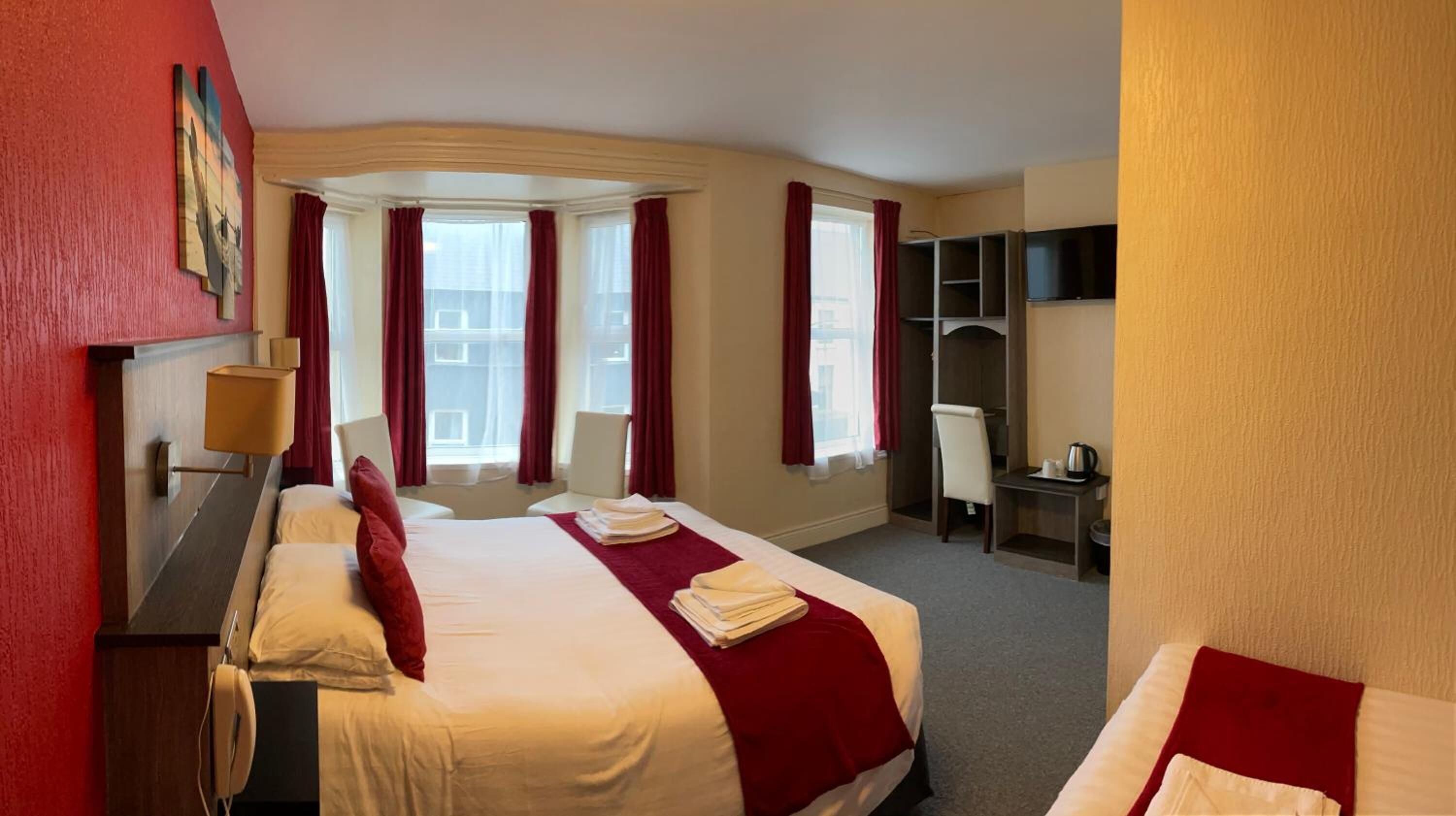 A hotel room with two beds, a desk, a chair, a TV, and a window with curtains.