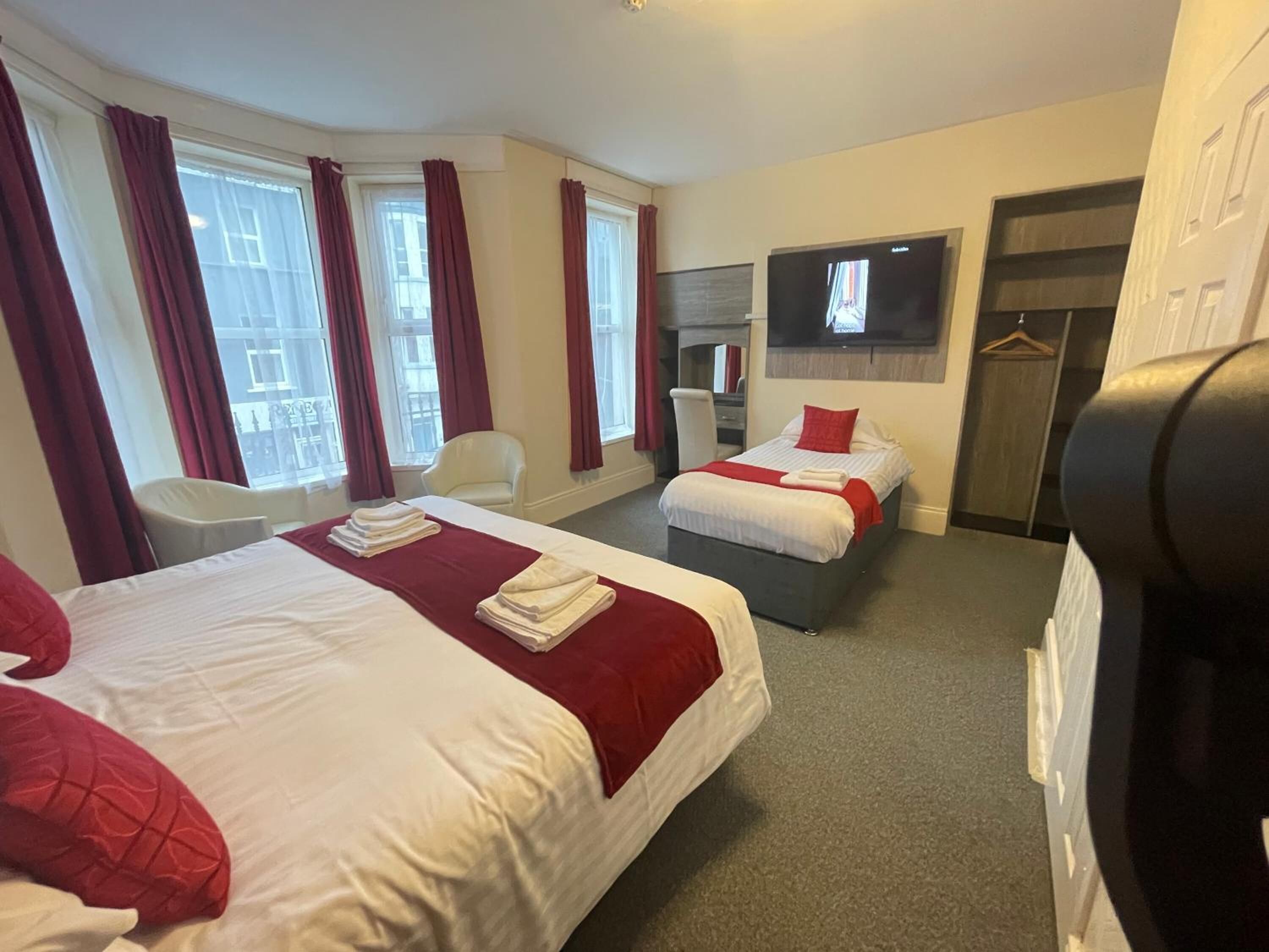 A hotel room with two beds, a desk, a chair, a TV, and a wardrobe.