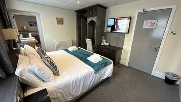 A hotel room with a large bed, a desk, a chair, a TV, and a door with a sign.