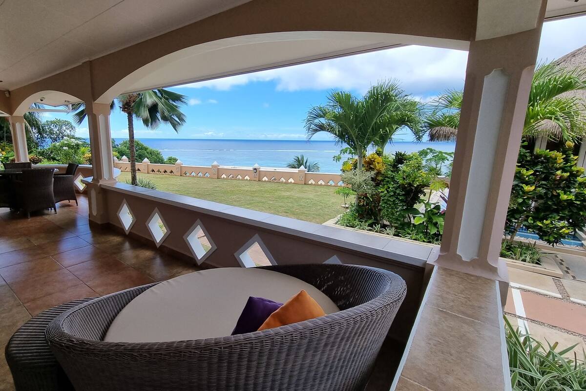 Un espacio de estar al aire libre cubierto con muebles de mimbre y vista al océano.