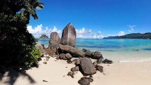 A beach with large rocks, clear turquoise water, and a distant island. - Au Fond De Mer View (Mahé Island)