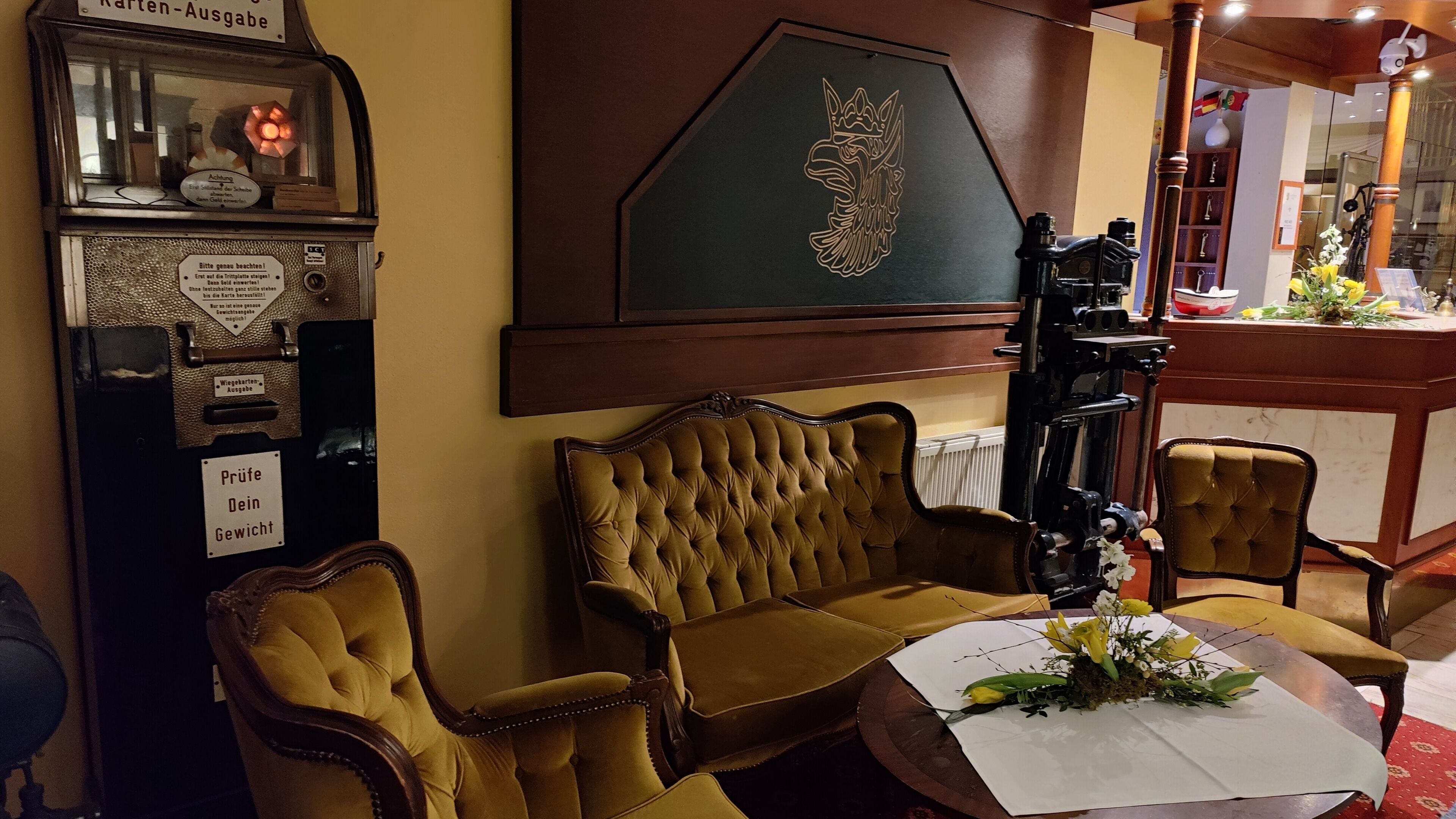 Una habitación con una máquina de escribir antigua, un sofá capitonado y una mesa con un arreglo floral.