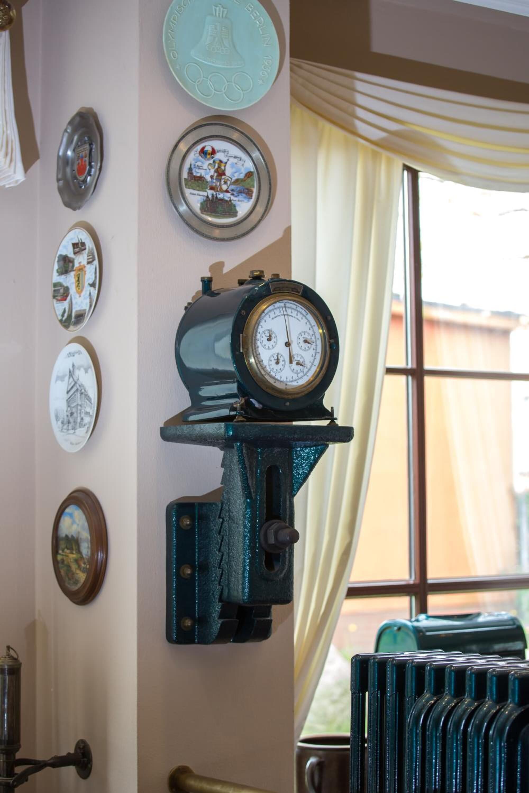 Eine Wand mit verschiedenen gerahmten Gegenständen, einer alten Uhr und einem Heizkörper.
