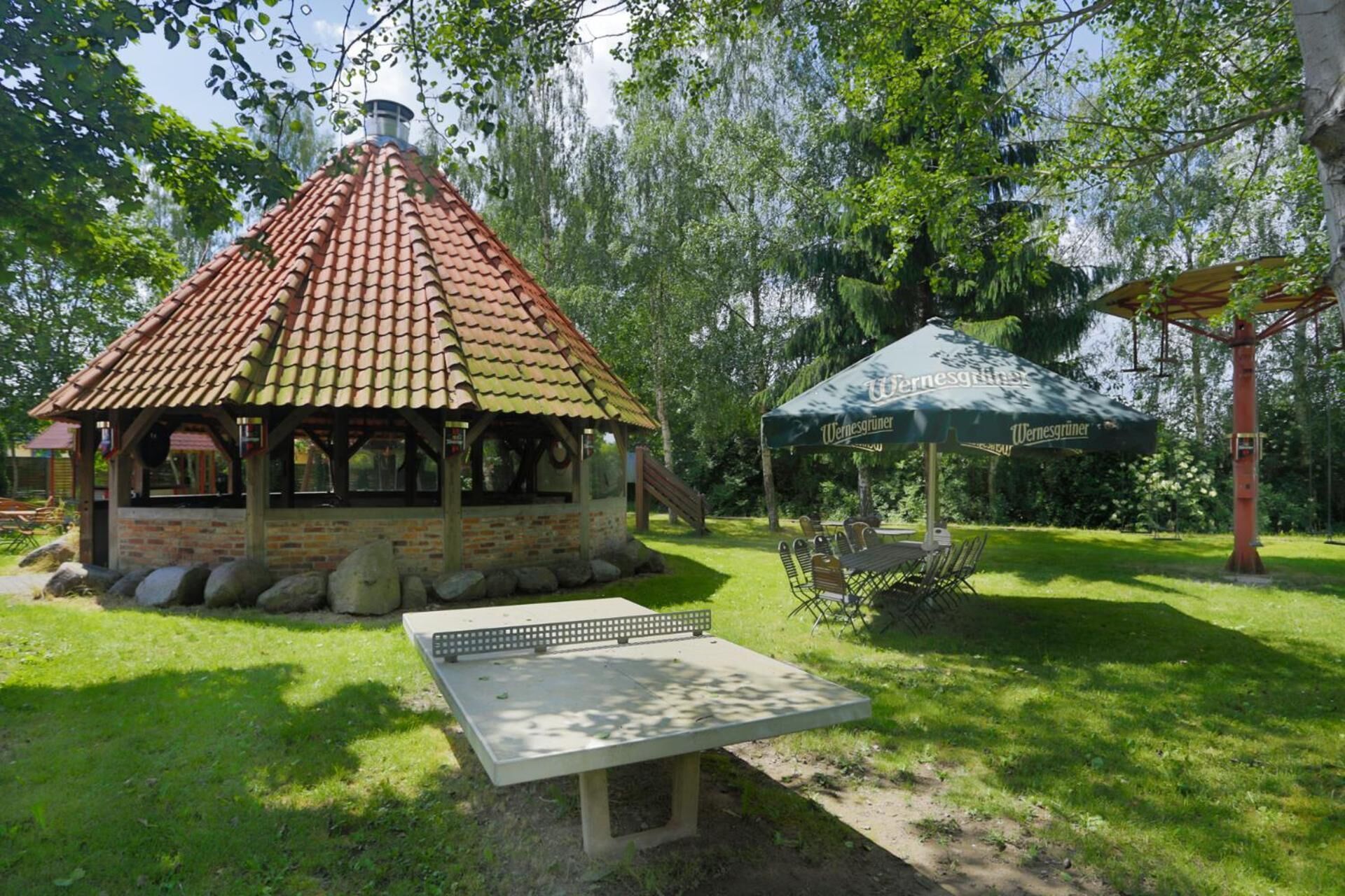 Ein Pavillon mit Ziegeldach, einem Tisch und einer Bank in einem Park.