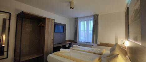 Una habitación de hotel con cama, escritorio, armario, televisor y ventana con cortinas.