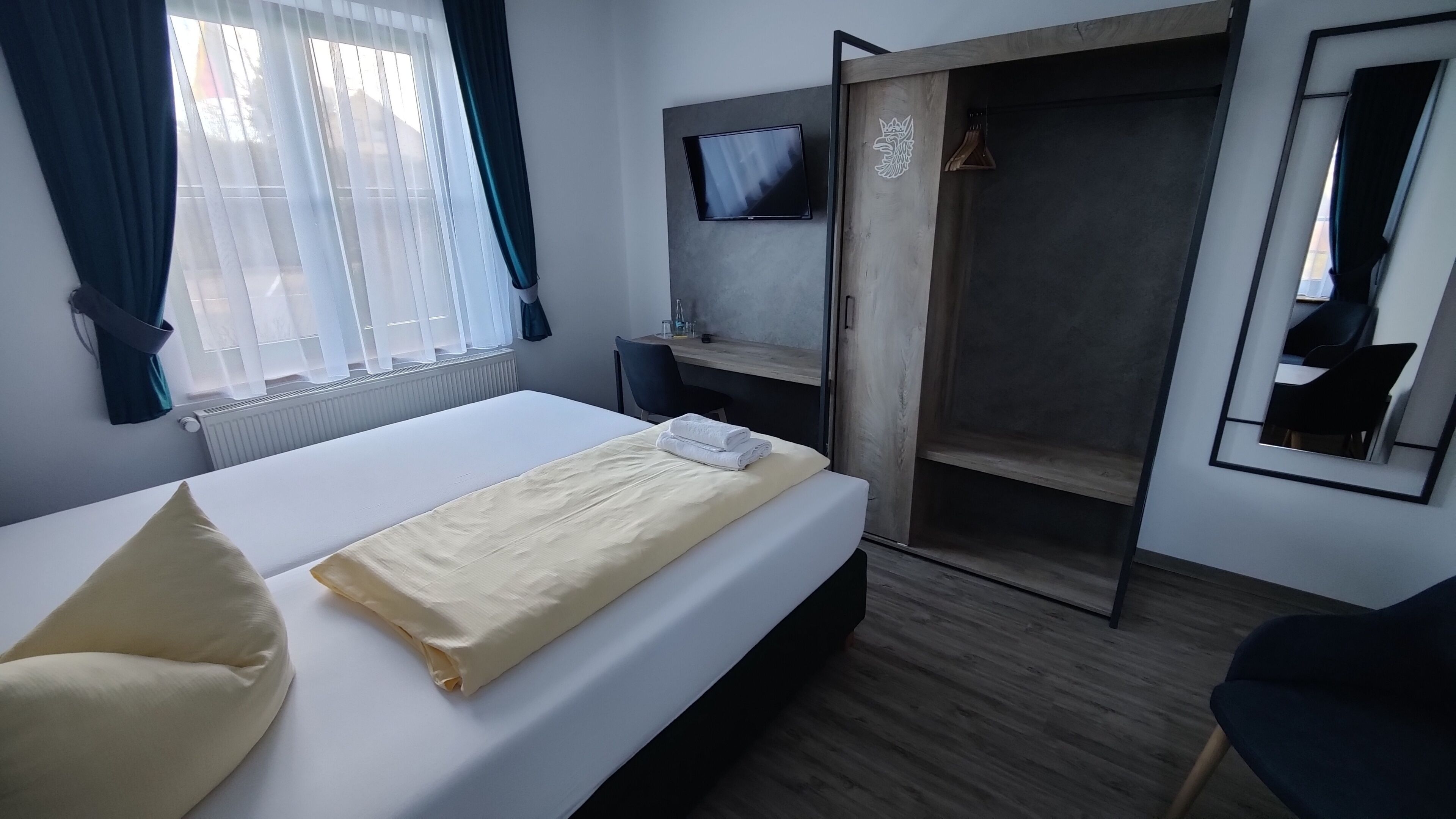 Et hotelværelse med seng, skrivebord, fjernsyn og garderobeskab.