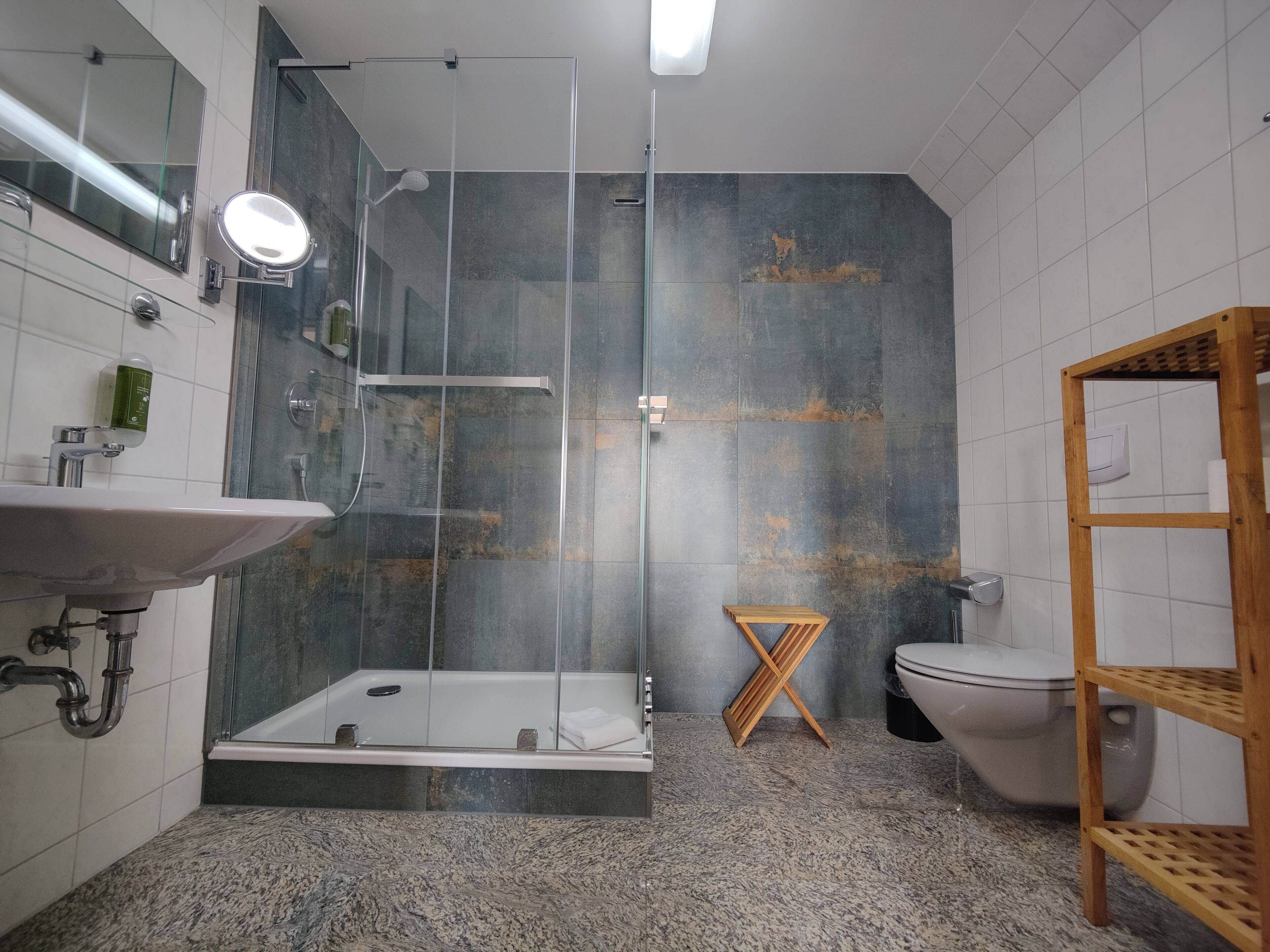 A modern bathroom with a glass-enclosed shower, a white sink, and a wooden shelf.