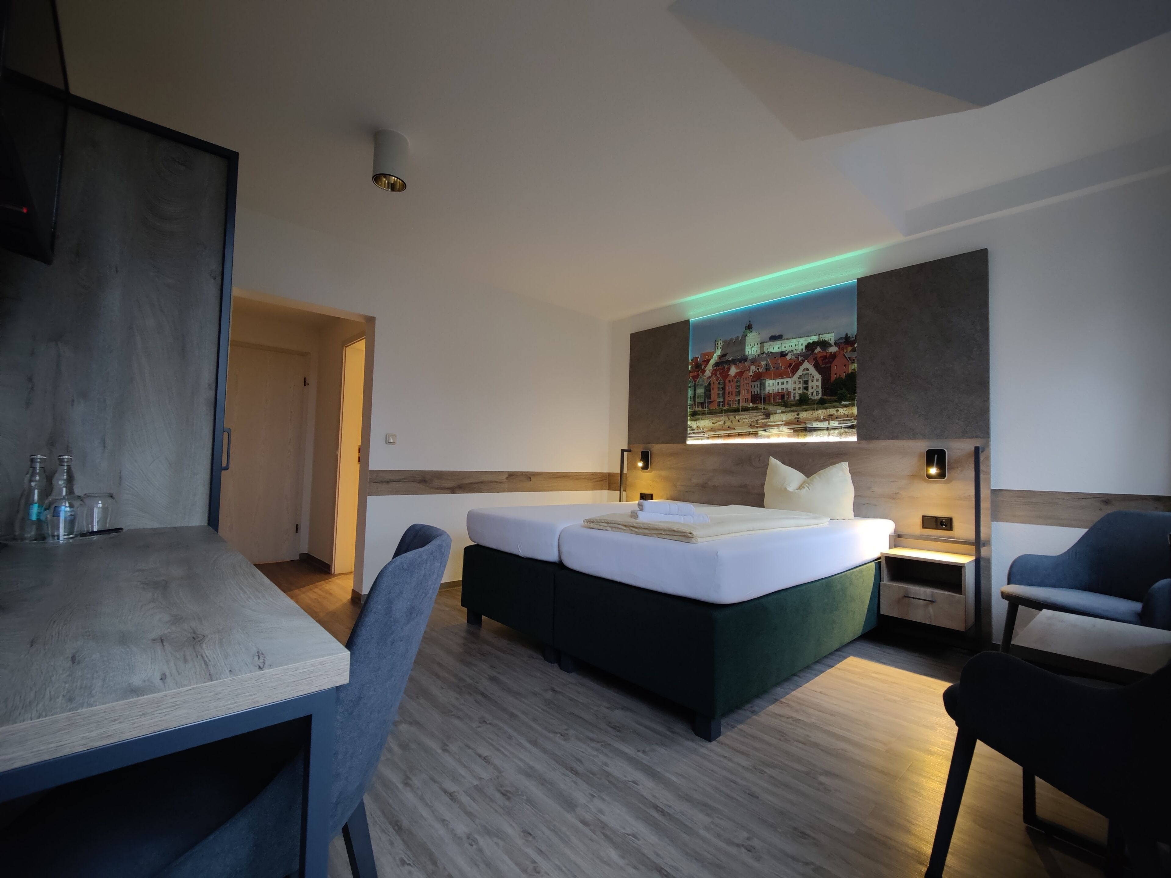 A modern hotel room with a wooden dining table, two single beds, a desk, and a nightstand.
