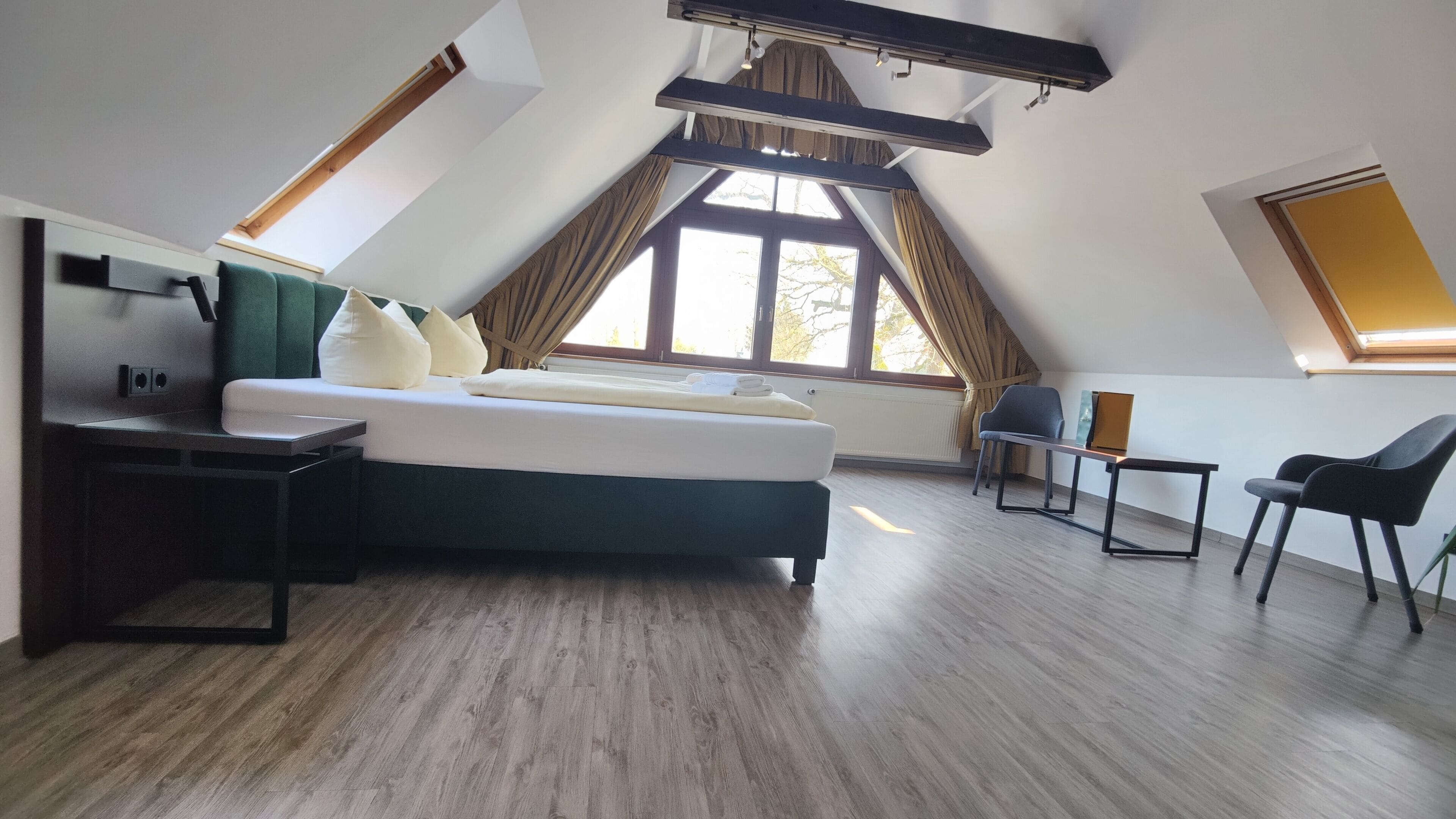 A modern bedroom with a bed, a desk, and a chair. There are large windows and a sloped ceiling.