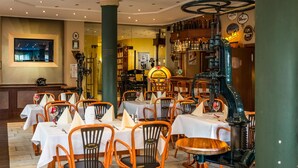 Un restaurante con mesas redondas y sillas de madera, una zona de bar con una grifería grande para cerveza, y una pared decorada con marcos y un reloj.