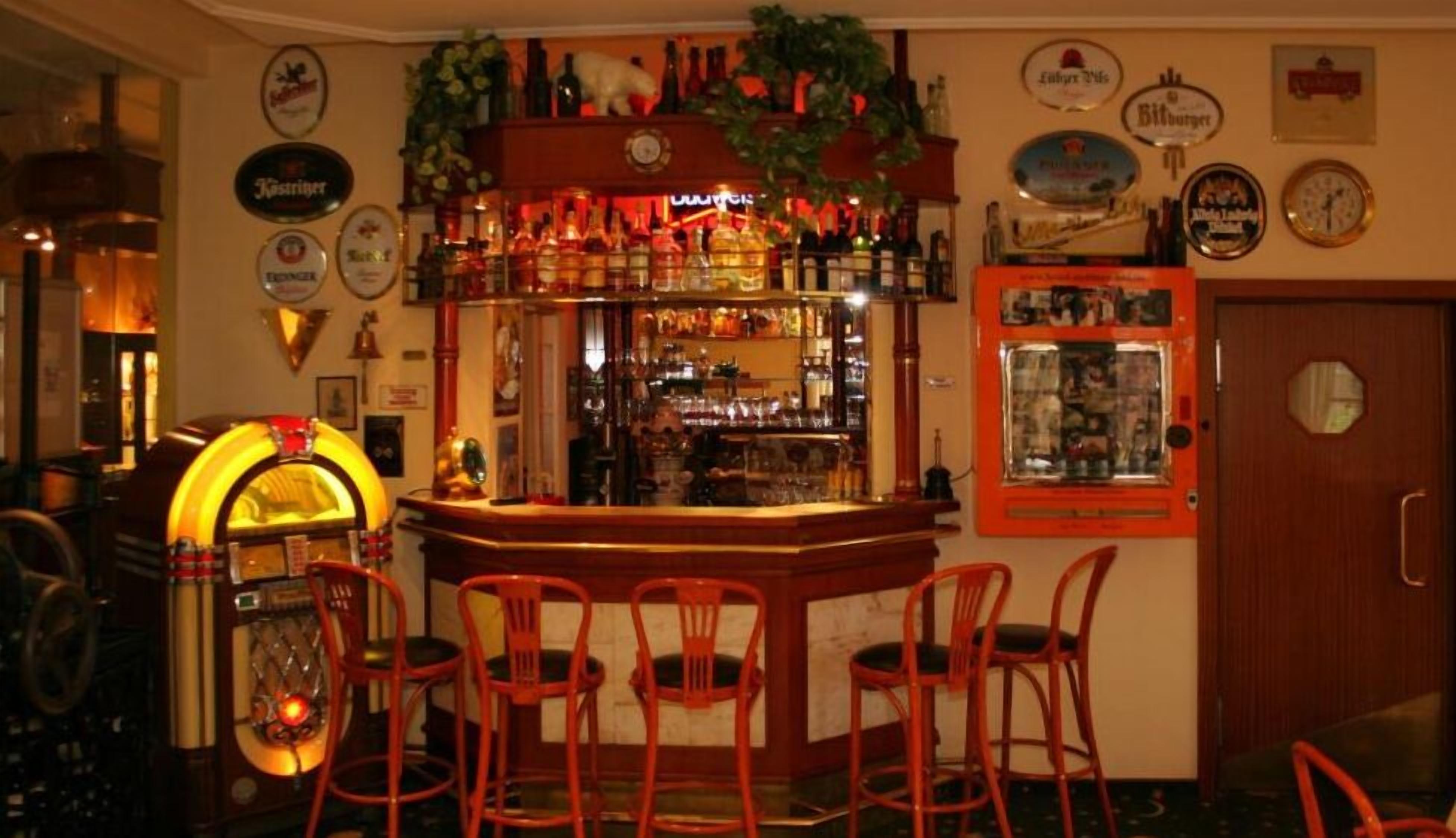 A bar area with a jukebox, red bar stools, and various liquor bottles on shelves.