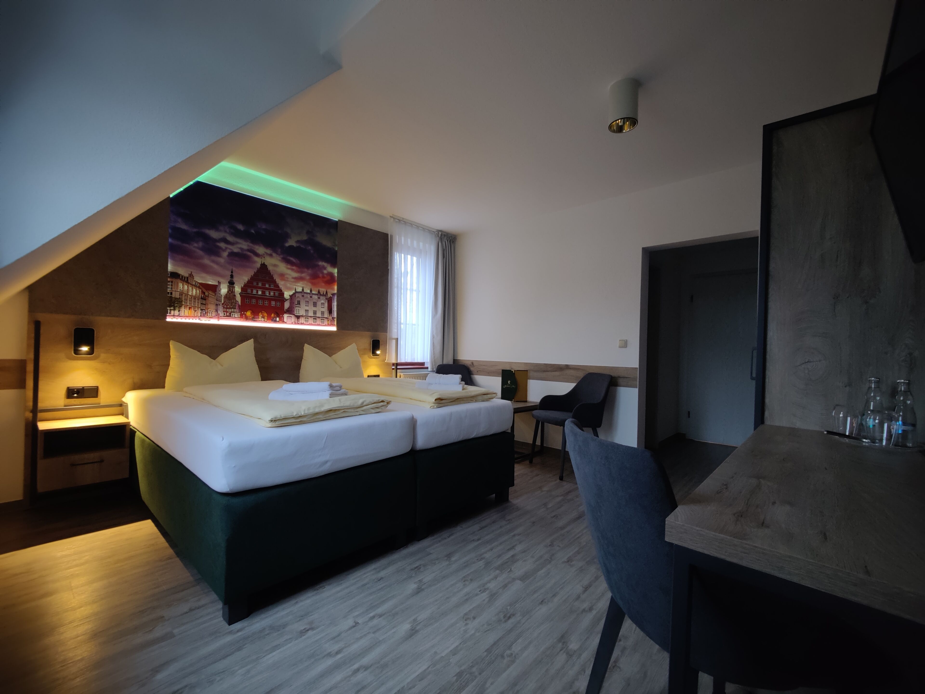Una habitación de hotel moderna con una cama, un escritorio y una silla. Hay un cuadro en la pared y una ventana con cortinas.