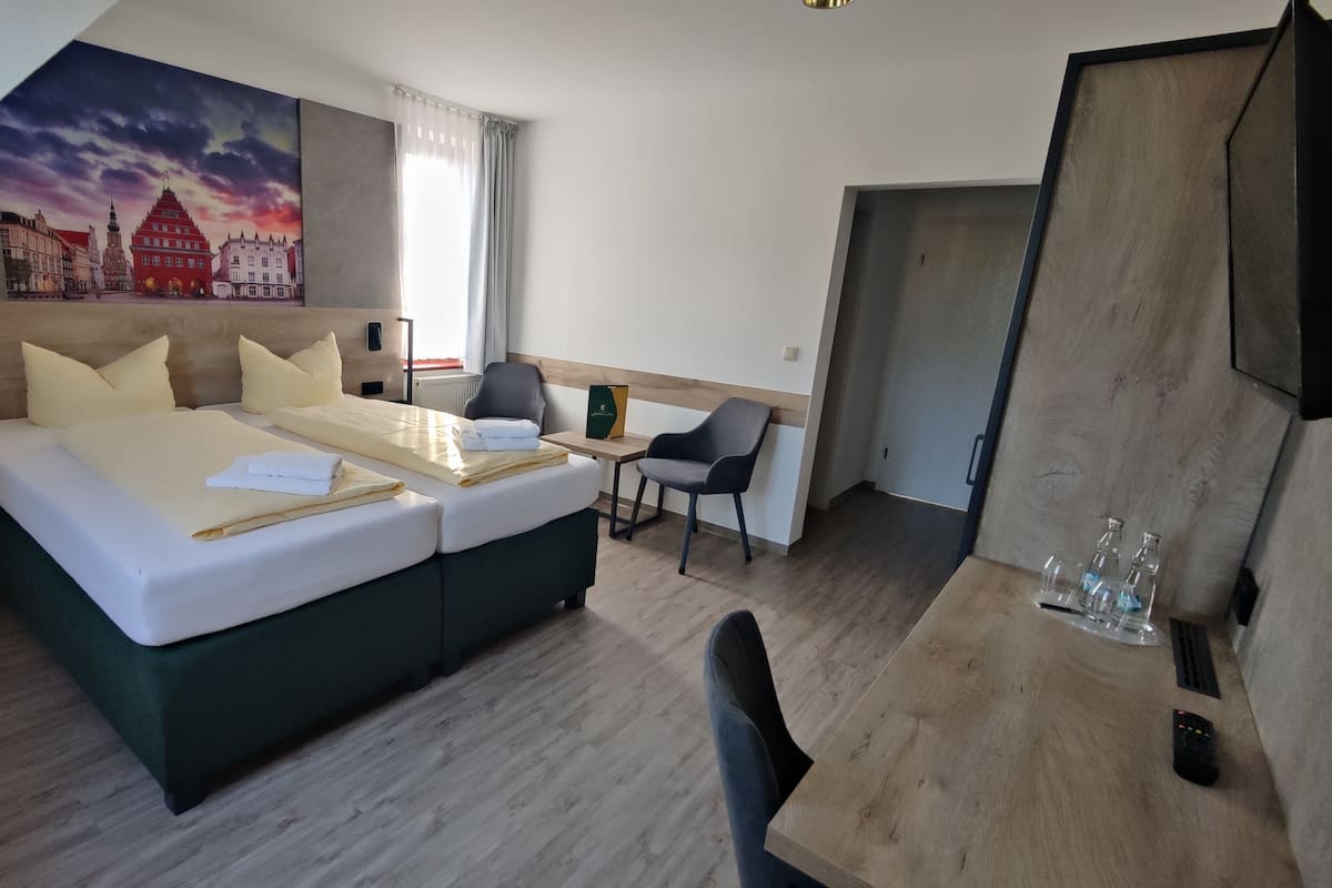 Una habitación de hotel moderna con una cama grande, un escritorio, una silla y un cuadro de un paisaje urbano.