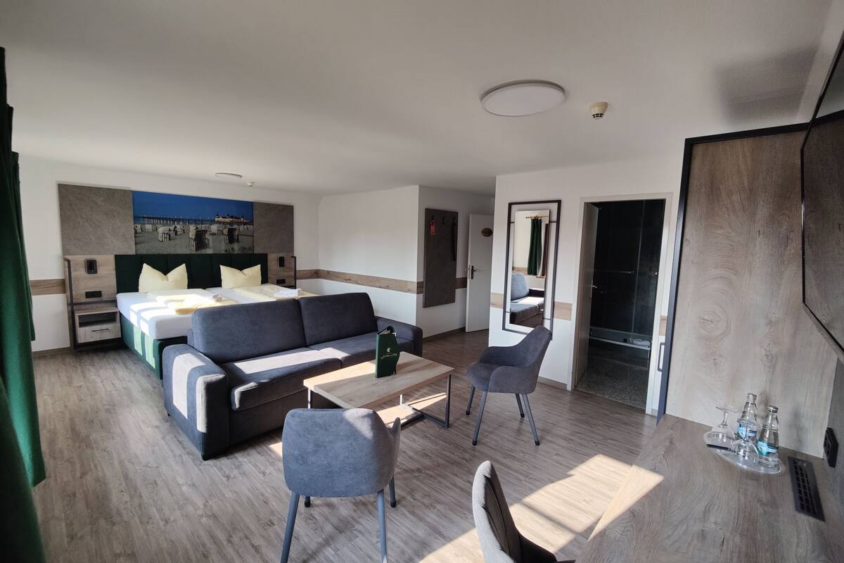 Una habitación de hotel moderna con cama, sofá, mesa de comedor y espejo.