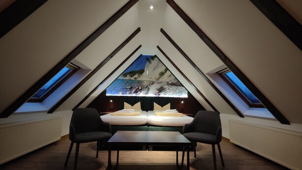 Un dormitorio acogedor en el ático con un tragaluz grande, una cama, dos sillones y una mesa.