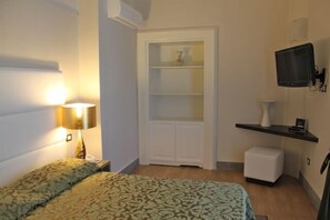 Ein Schlafzimmer mit Bett, Nachttischlampe, Kleiderschrank, Fernseher und einem kleinen weißen Schrank.