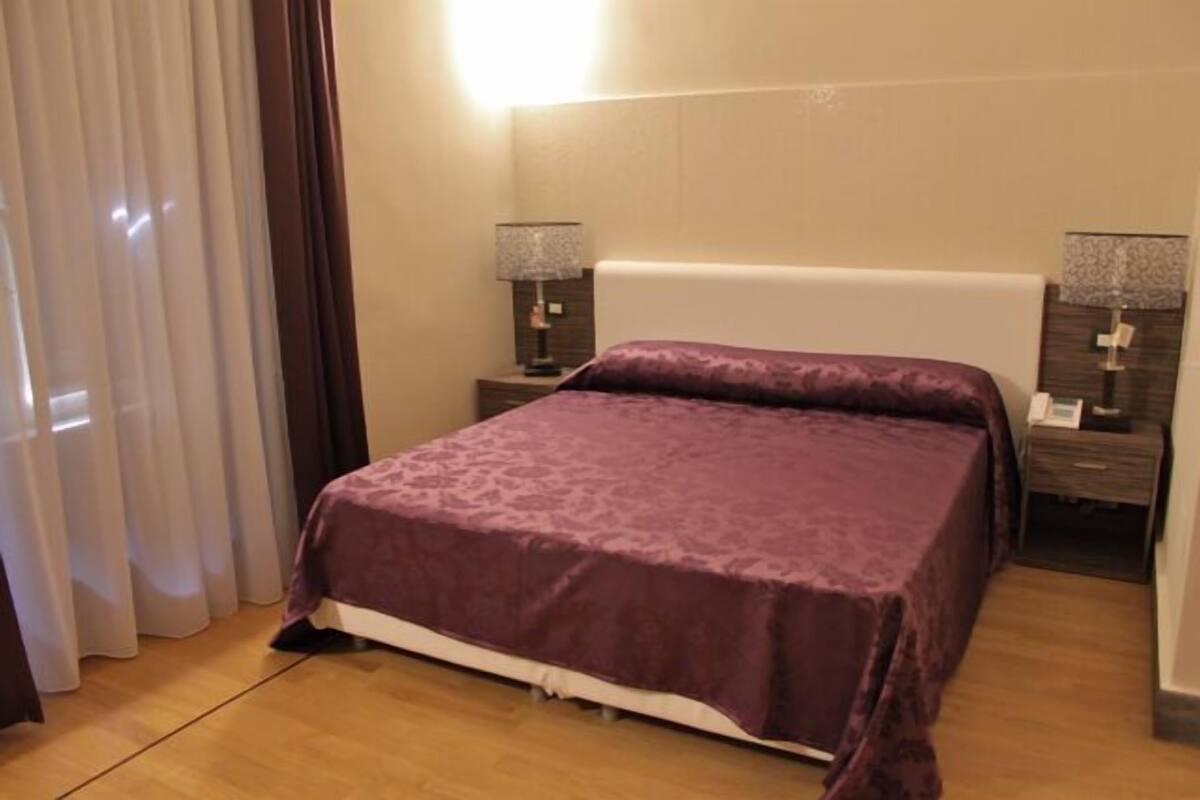 A hotel room with a bed, two bedside tables, and a nightstand.