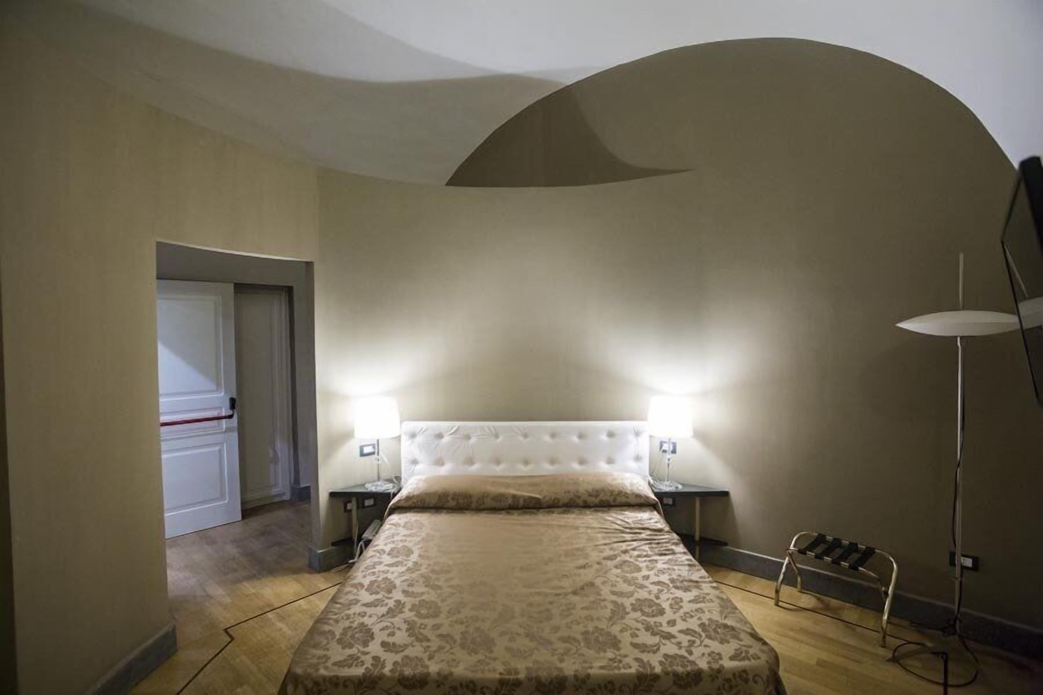 Ein Schlafzimmer mit einem gepolsterten Kopfteil, einer gemusterten Bettdecke, Nachttischlampen und einer Stehlampe.
