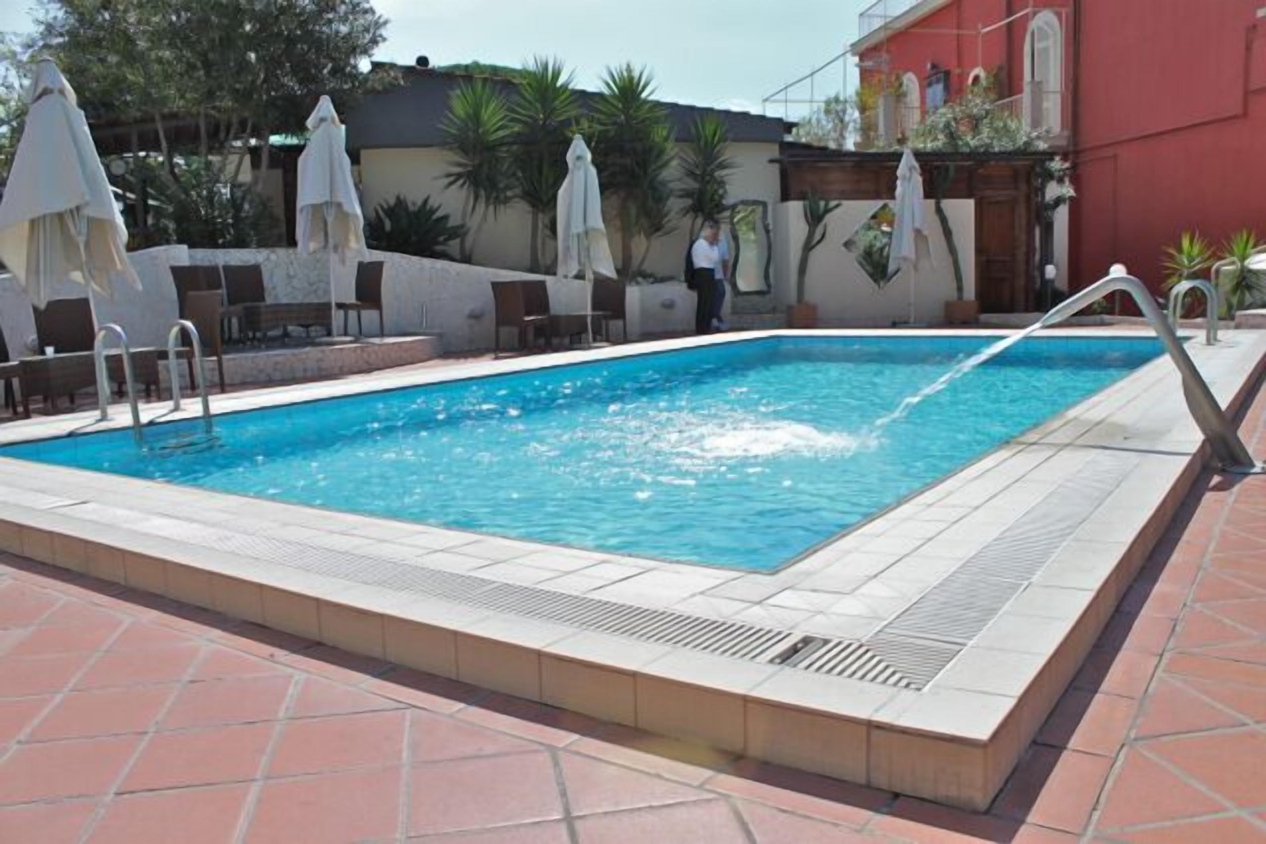 A rectangular swimming pool with a tiled deck, surrounded by lounge chairs and umbrellas.
