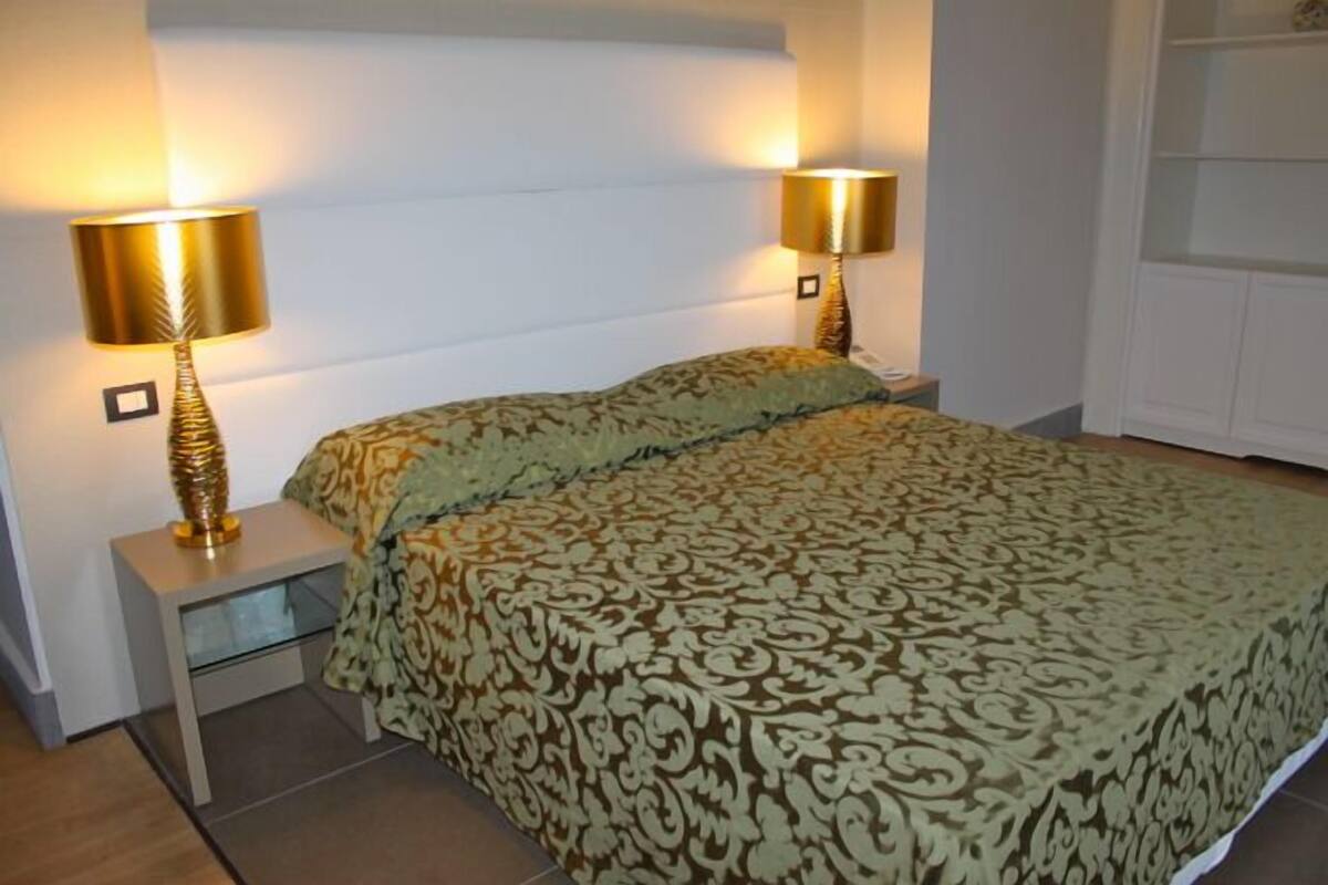 A bedroom with a bed, two bedside lamps, a nightstand, and a wardrobe.
