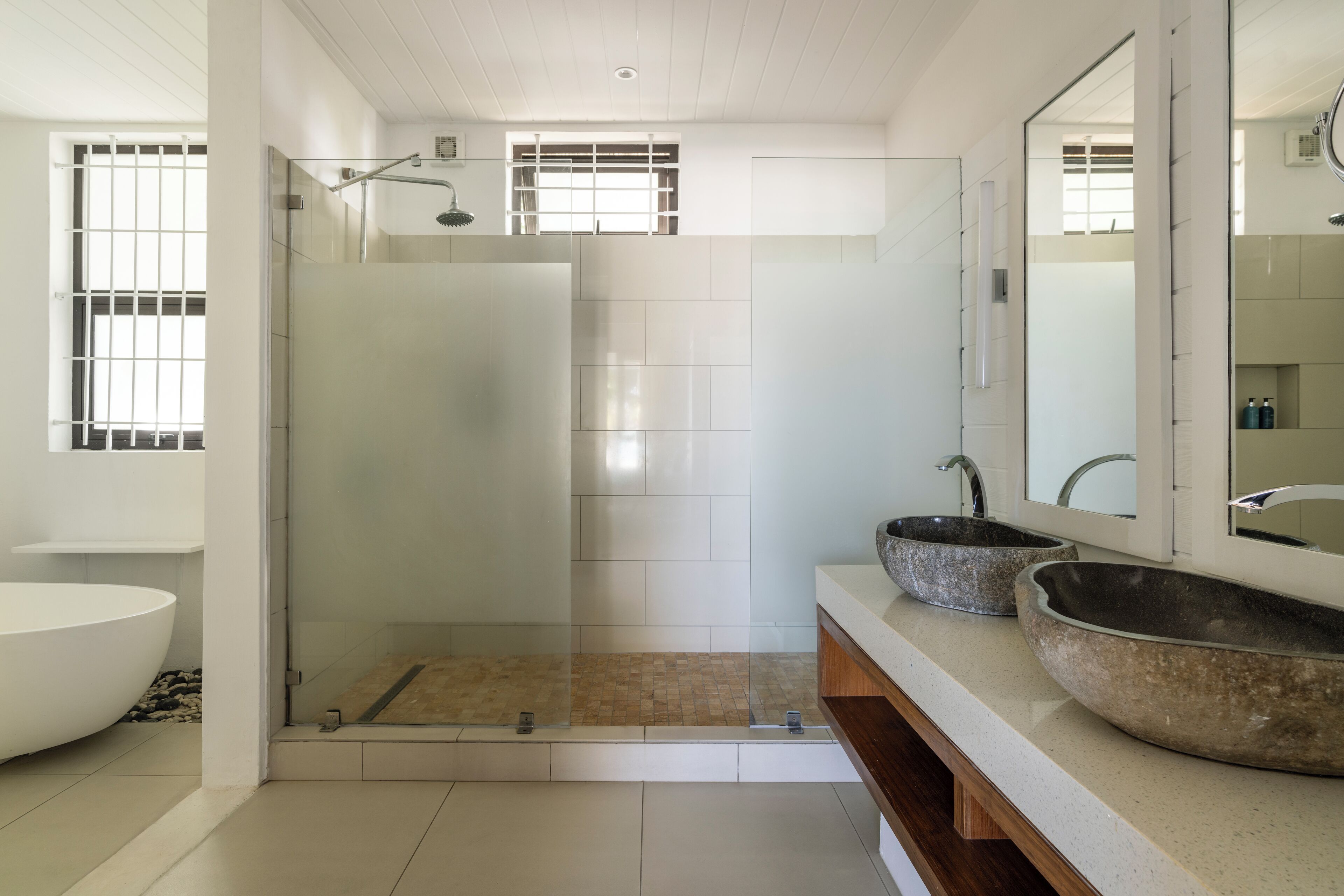 Ein modernes Badezimmer mit einer gläsernen Duschkabine, einer freistehenden Badewanne und zwei Aufsatzwaschbecken.