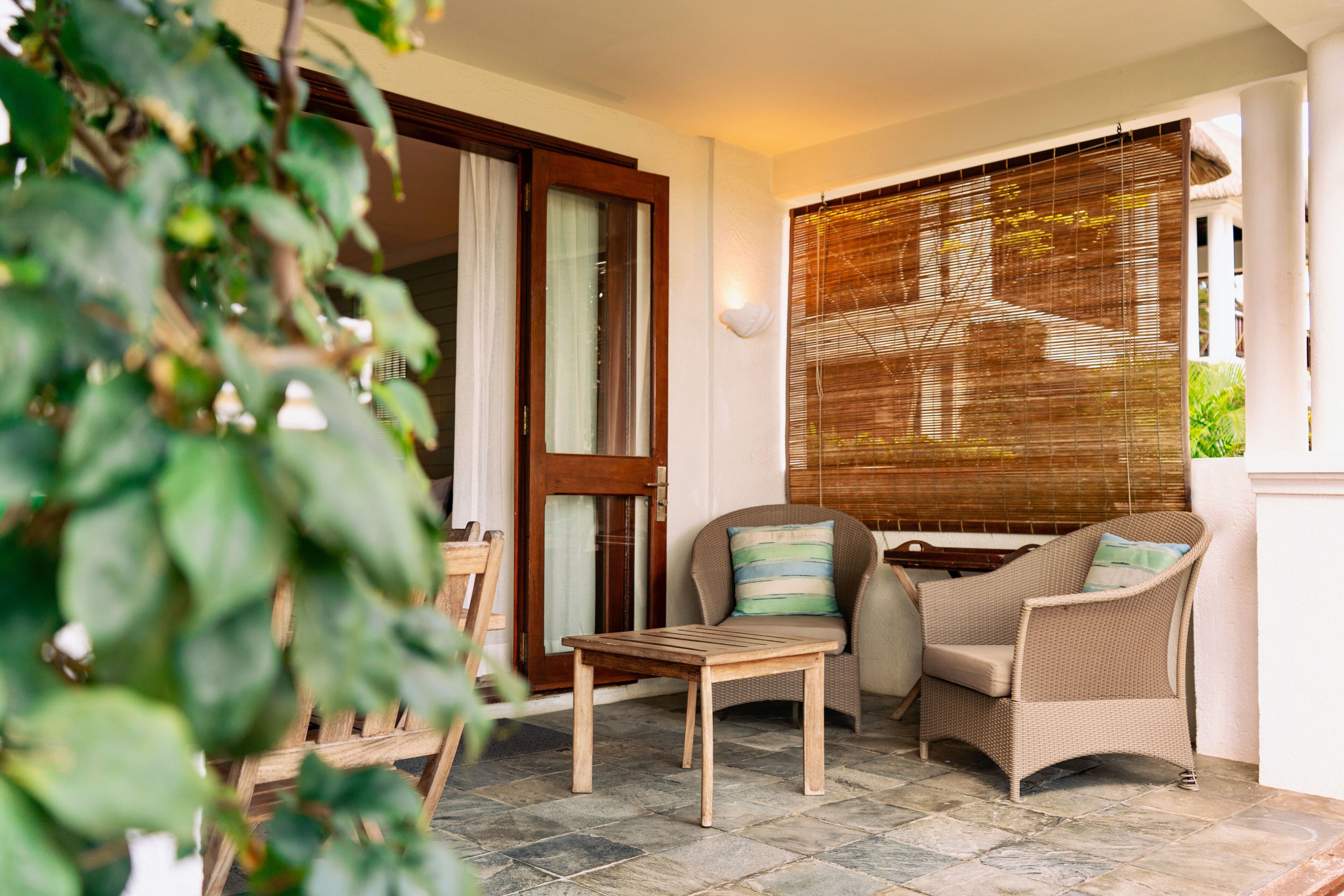 A room with a wooden table and two wicker chairs, a sliding glass door, and a bamboo blind.