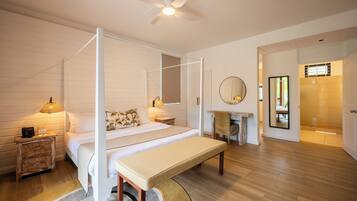 Un dormitorio con cama con dosel, una banca, una mesita de noche con lámpara, un espejo y vistas al baño.