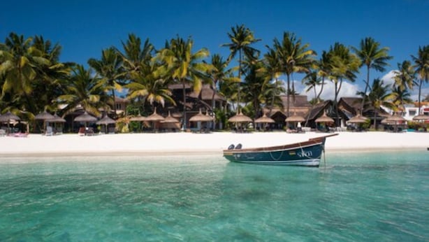 A beach with clear turquoise water, a boat, and overwater bungalows with thatched roofs. - Constance Sakoa Boutik (Trou aux Biches)