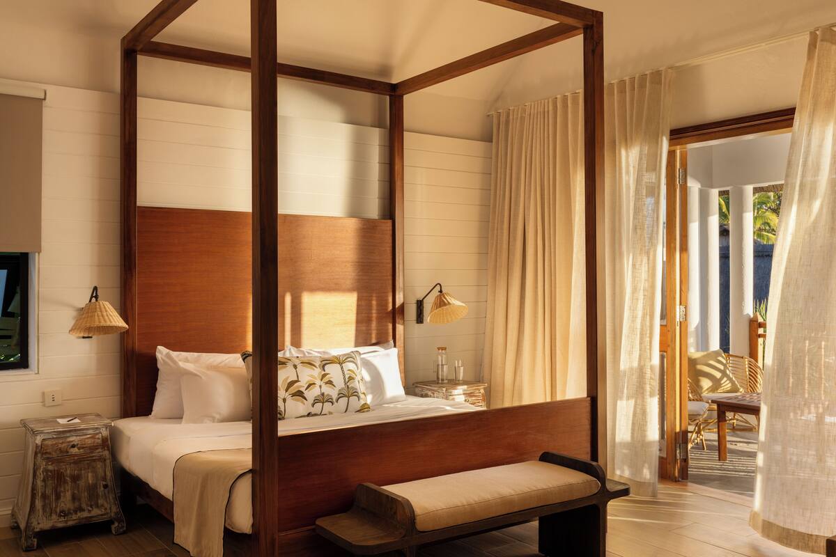 A four-poster bed with a wooden headboard, a bedside table with a lamp, and a bench at the foot of the bed.