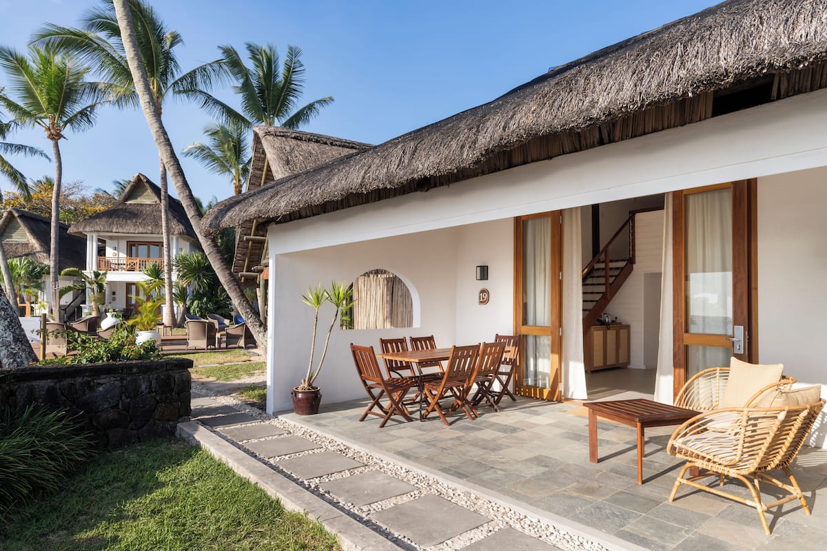 A resort with a thatched-roof building, outdoor seating, and palm trees.